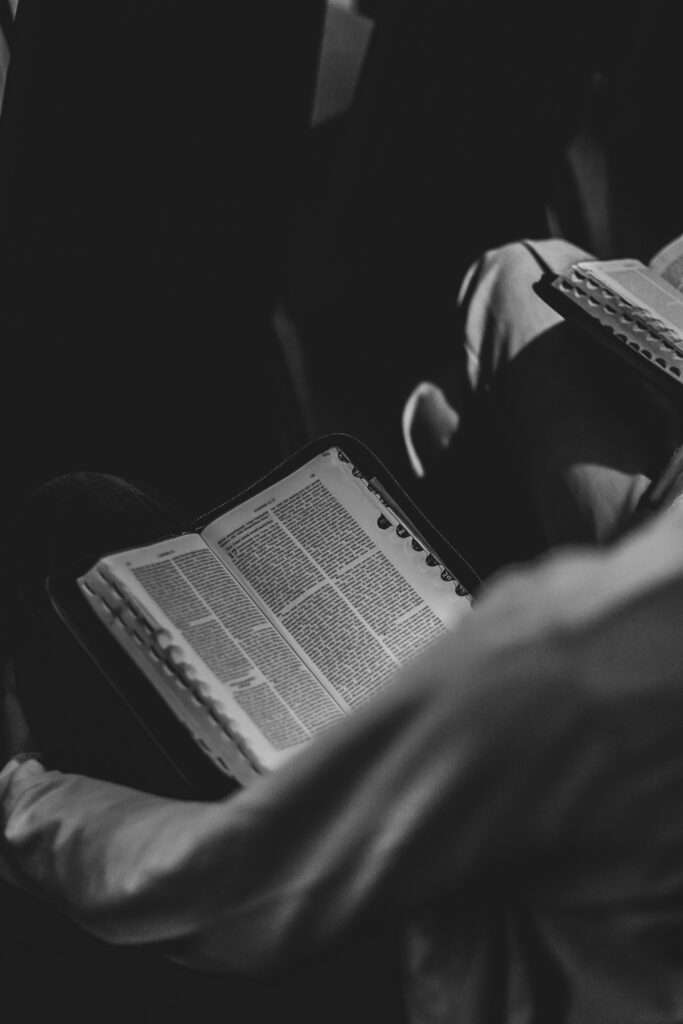 Isn’t He worthy? Black and white photo of a person reading an open Bible, focused on the book.